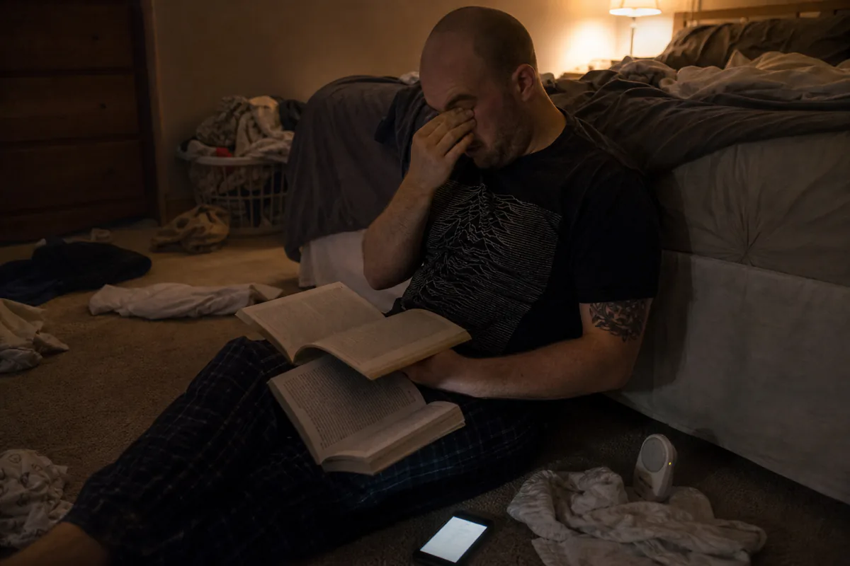 A parent sitting on the bedroom floor at night with two open books and a baby monitor